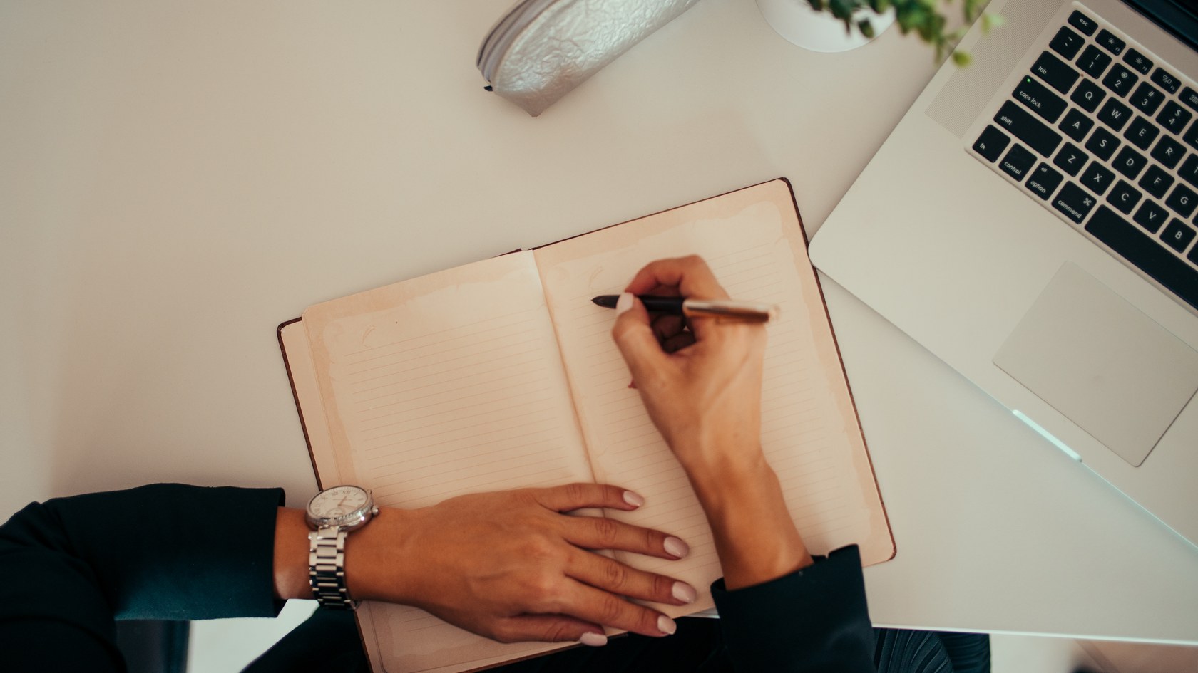 Person working at a desk with a notebook, laptop and smartphone